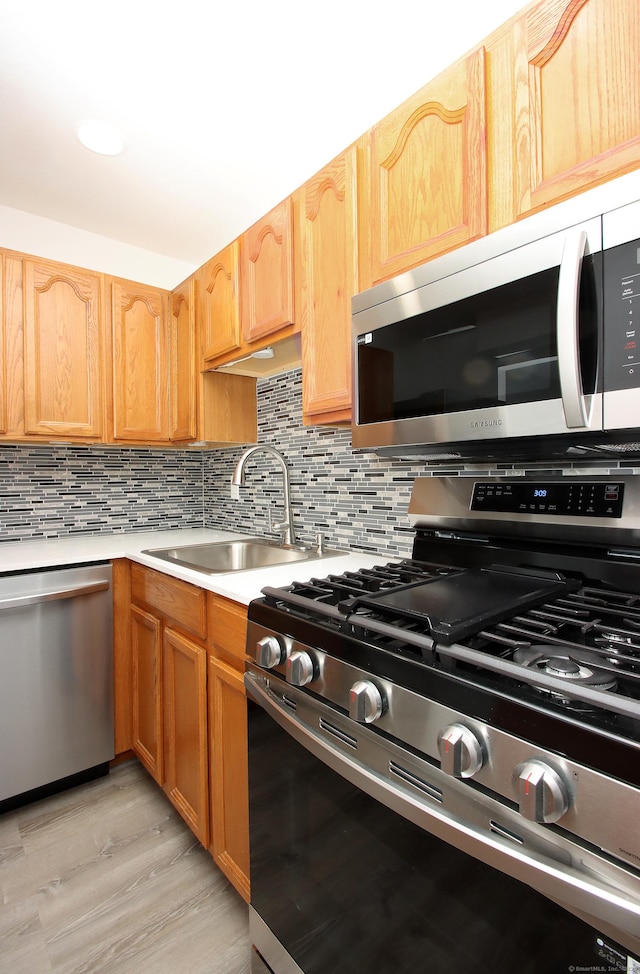 kitchen featuring tasteful backsplash, light wood-style flooring, stainless steel appliances, light countertops, and a sink