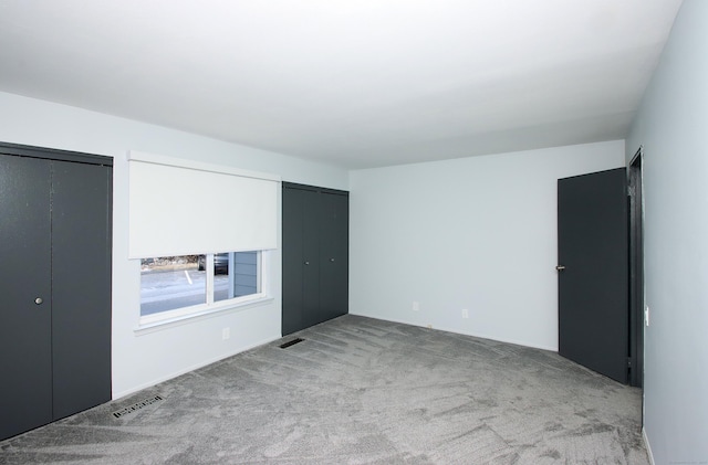 unfurnished bedroom with multiple closets, visible vents, and light colored carpet