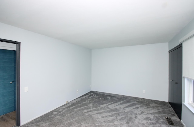 unfurnished bedroom featuring visible vents, dark carpet, and a closet