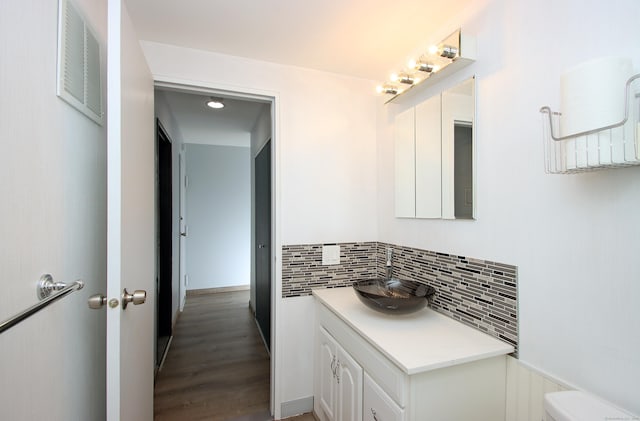 half bath with visible vents, backsplash, toilet, vanity, and wood finished floors