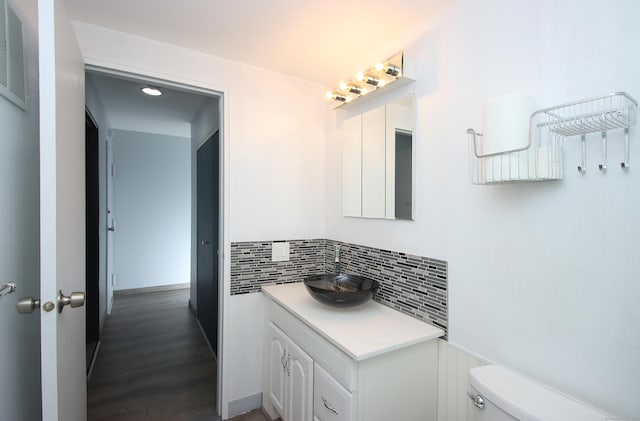 half bathroom featuring tasteful backsplash, visible vents, toilet, vanity, and wood finished floors