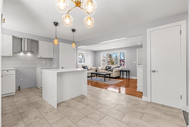 kitchen with white cabinets, decorative backsplash, decorative light fixtures, light countertops, and wall chimney range hood