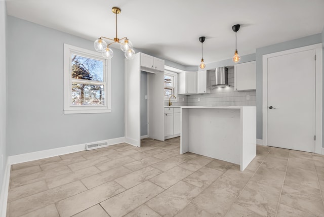 kitchen featuring white cabinetry, visible vents, light countertops, wall chimney range hood, and tasteful backsplash