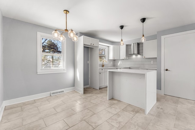 kitchen with decorative backsplash, light countertops, wall chimney range hood, white cabinetry, and a sink