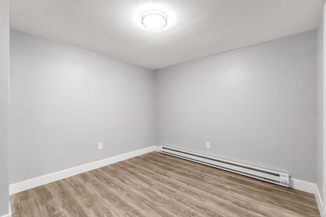 unfurnished room featuring a baseboard radiator, baseboards, and wood finished floors