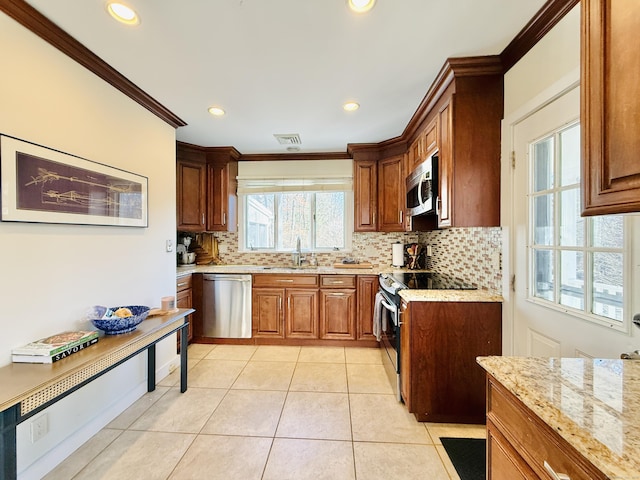 kitchen with light tile patterned floors, ornamental molding, light stone counters, stainless steel appliances, and a sink