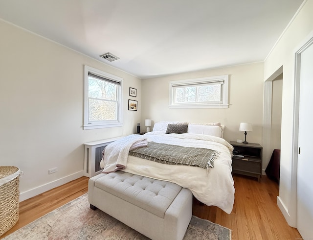 bedroom with multiple windows, visible vents, baseboards, and wood finished floors