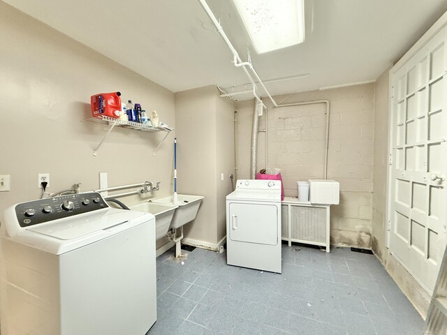 clothes washing area featuring concrete block wall, washer and clothes dryer, a sink, and tile patterned floors