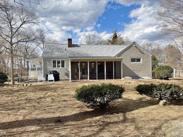 back of house with a sunroom, a chimney, and roof with shingles