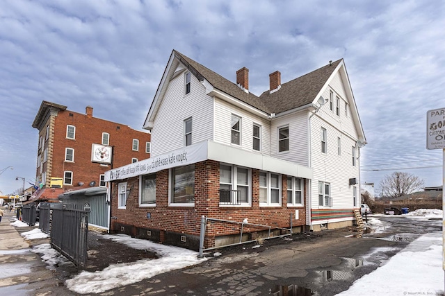 snow covered property with brick siding, a chimney, and a shingled roof