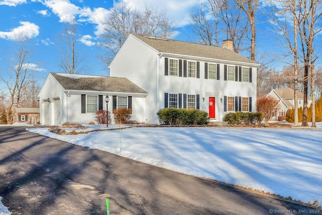 colonial-style house with driveway, a chimney, and an attached garage