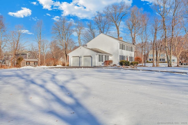 snow covered property with a garage and a chimney