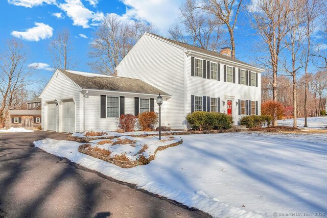 view of front facade featuring driveway, a chimney, and an attached garage