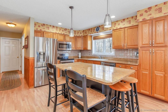 kitchen featuring stainless steel appliances, a sink, a textured ceiling, light stone countertops, and light wood-type flooring