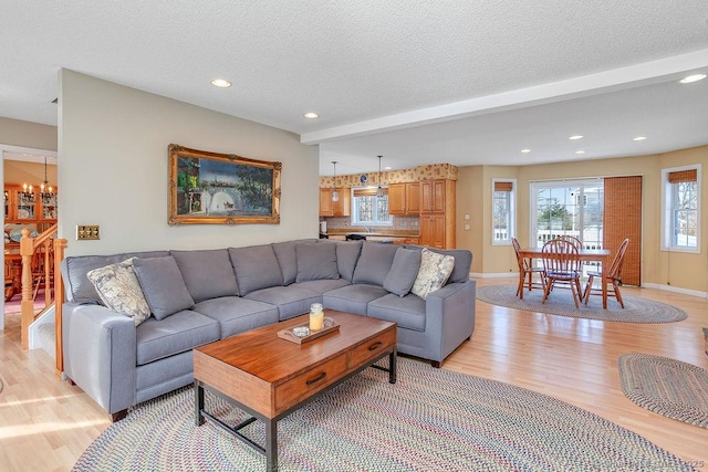 living room with a chandelier, light wood finished floors, a textured ceiling, and baseboards