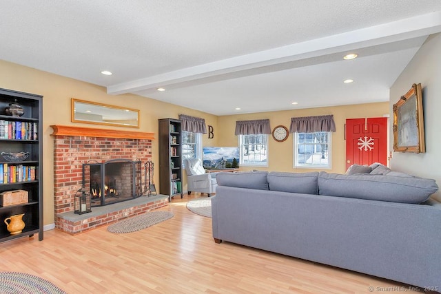 living area featuring a textured ceiling, recessed lighting, wood finished floors, a brick fireplace, and beam ceiling