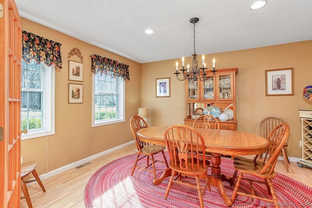 dining room with a notable chandelier, visible vents, light wood-style flooring, a textured ceiling, and baseboards