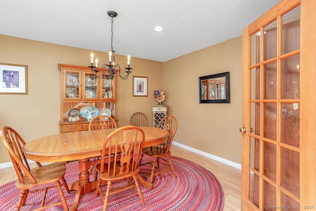 dining area featuring light wood-style floors, a textured ceiling, baseboards, and an inviting chandelier