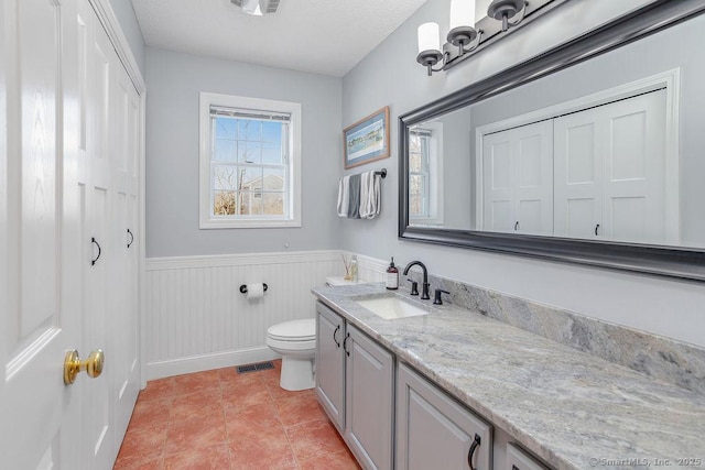 bathroom featuring tile patterned flooring, toilet, a wainscoted wall, vanity, and visible vents