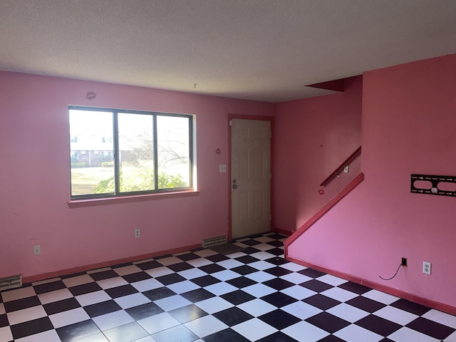 empty room with a textured ceiling, light floors, stairway, and visible vents