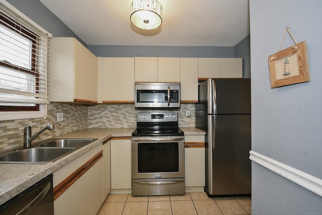 kitchen featuring cream cabinets, light tile patterned flooring, stainless steel appliances, a sink, and decorative backsplash