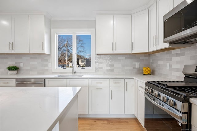 kitchen with appliances with stainless steel finishes, light stone counters, light wood-style floors, white cabinetry, and a sink