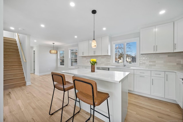 kitchen with white cabinetry, a sink, light wood-style flooring, and a kitchen bar