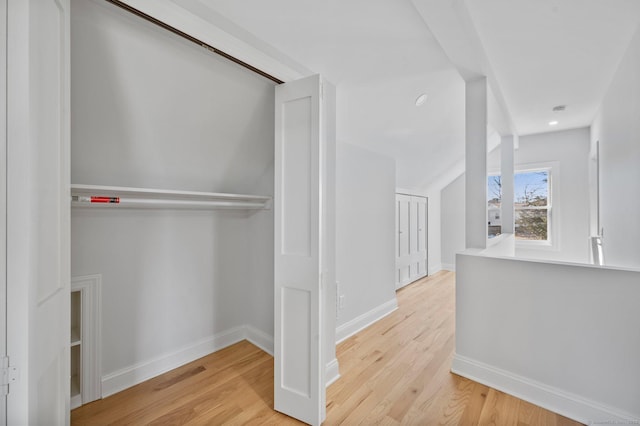 hallway featuring vaulted ceiling, wood finished floors, and baseboards