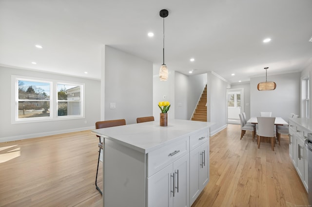 kitchen with pendant lighting, light wood-style floors, ornamental molding, a kitchen island, and a kitchen breakfast bar