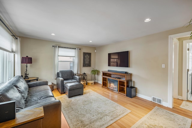 living area with a glass covered fireplace, visible vents, baseboards, and wood finished floors