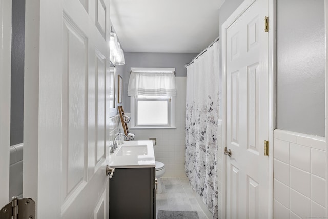 bathroom featuring toilet, wainscoting, vanity, and tile walls