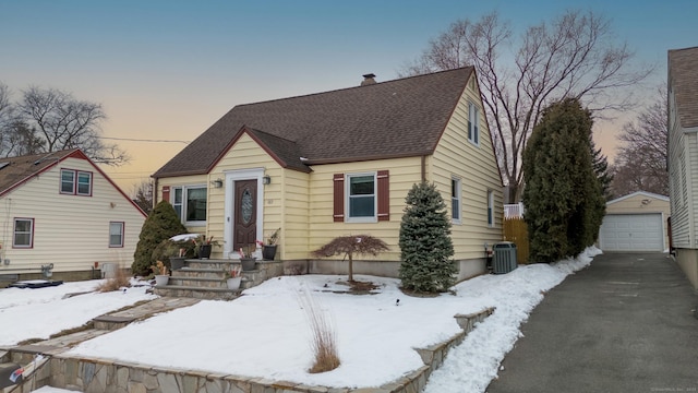 view of front of house with central air condition unit, roof with shingles, a detached garage, and an outdoor structure