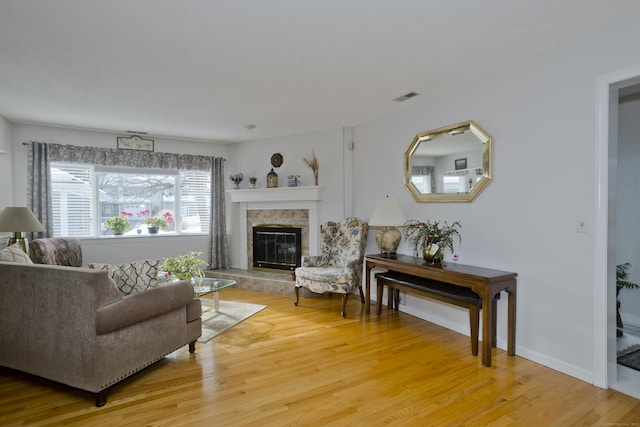 living area featuring light wood-style flooring, visible vents, baseboards, and a glass covered fireplace