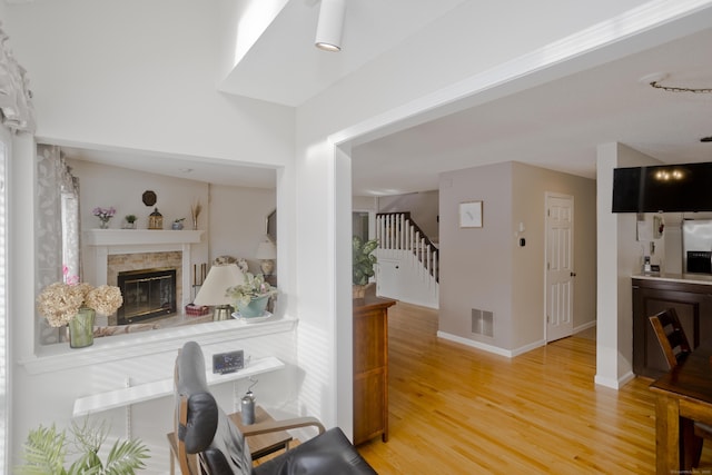 living area with baseboards, visible vents, a glass covered fireplace, stairs, and light wood-style floors