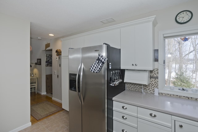 kitchen with light tile patterned floors, light countertops, white cabinetry, stainless steel refrigerator with ice dispenser, and backsplash