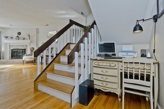 stairway with visible vents, wood finished floors, and a glass covered fireplace