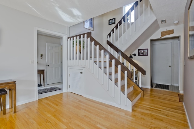 stairs featuring visible vents, a textured ceiling, baseboards, and wood finished floors