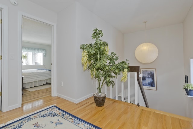 hallway featuring baseboards, wood finished floors, and an upstairs landing