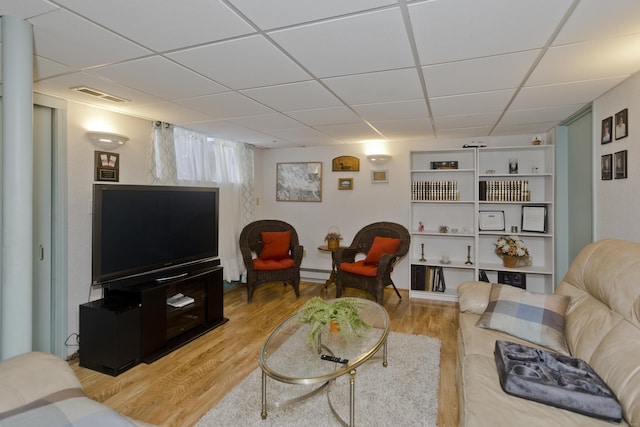 living room with a drop ceiling, baseboard heating, light wood-type flooring, and visible vents