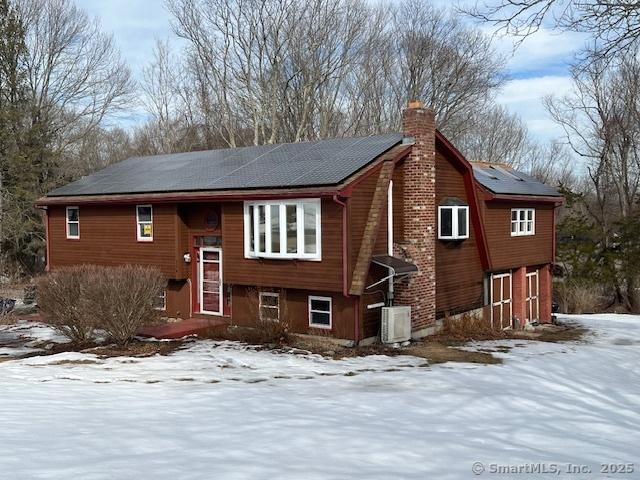 view of front of house featuring a chimney, roof mounted solar panels, and central AC unit