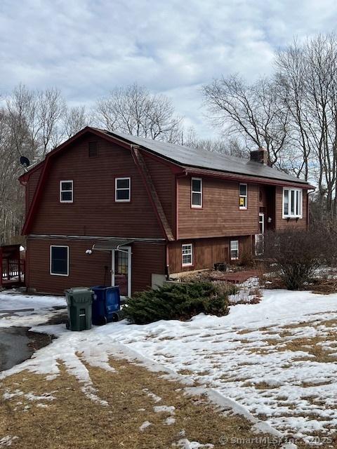 snow covered back of property with a chimney and a gambrel roof