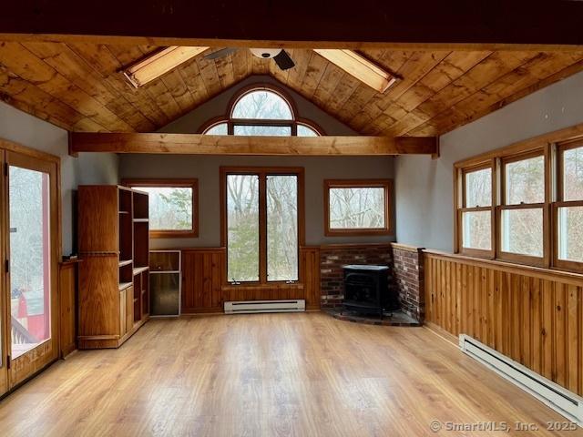 unfurnished living room with a wood stove, a baseboard heating unit, and wainscoting