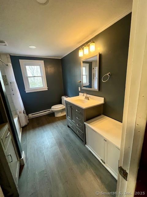 full bathroom with toilet, a baseboard heating unit, wood finished floors, vanity, and crown molding