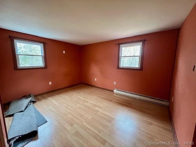 spare room with a baseboard radiator, light wood-style flooring, and baseboards