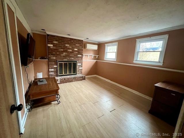 living area featuring a brick fireplace, crown molding, a wall mounted AC, and wood finished floors