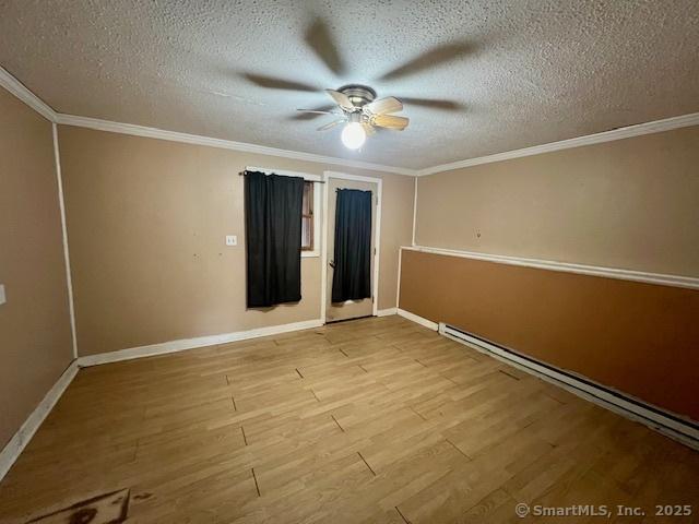 empty room with a baseboard heating unit, a textured ceiling, wood finished floors, and crown molding