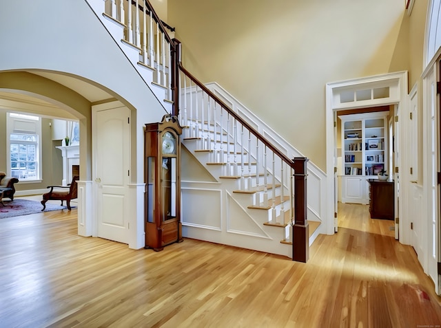 stairway with arched walkways, a fireplace, wood finished floors, and a towering ceiling