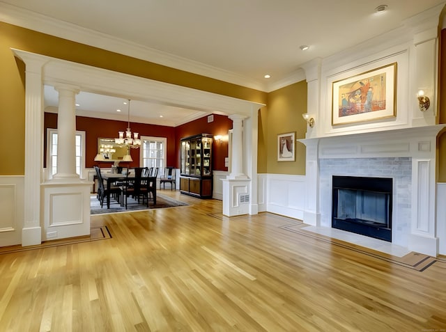 unfurnished living room featuring a decorative wall, light wood-style flooring, crown molding, and decorative columns