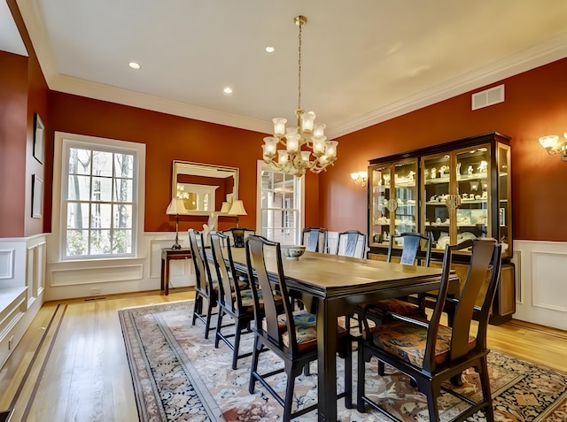 dining room with light wood-type flooring, visible vents, a wainscoted wall, a notable chandelier, and ornamental molding