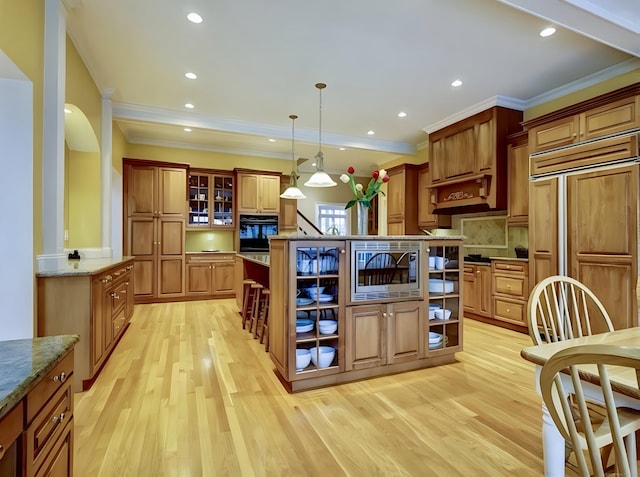 kitchen with light stone countertops, light wood finished floors, glass insert cabinets, and built in appliances